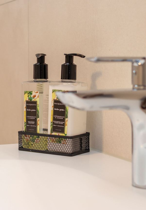 Waschbecken auf dem zwei Seifenspender stehen in einem schwarzen Metalkorb.