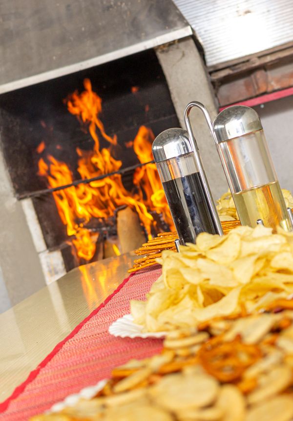 Feuerstelle mit Feuer davor ein Tisch gedeckt mit Essig und Öl sowie Solleti und Chips im Papptellern